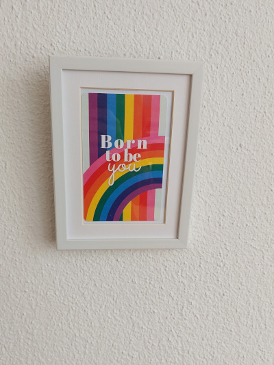 Gerahmtes Wandbild mit dem Text 'Born to be you' in bunten Buchstaben auf regenbogenfarbenem Hintergrund mit Streifen und Regenbogen-Motiv